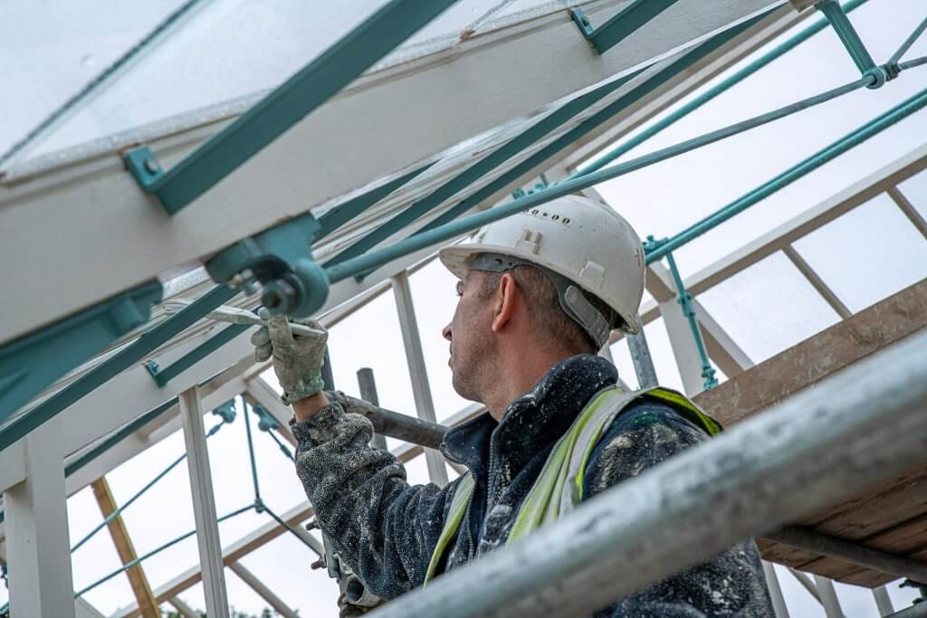 A worker painting the ironwork inside the glasshouses. Picture featuring in the glasshouses restoration