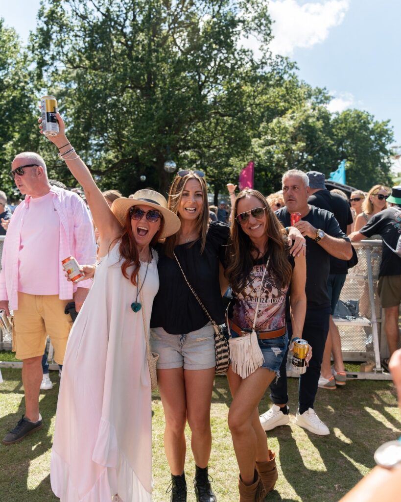 a group of three women post for a photo amongst the crowd, all with big smiles and one with her arm in the air.