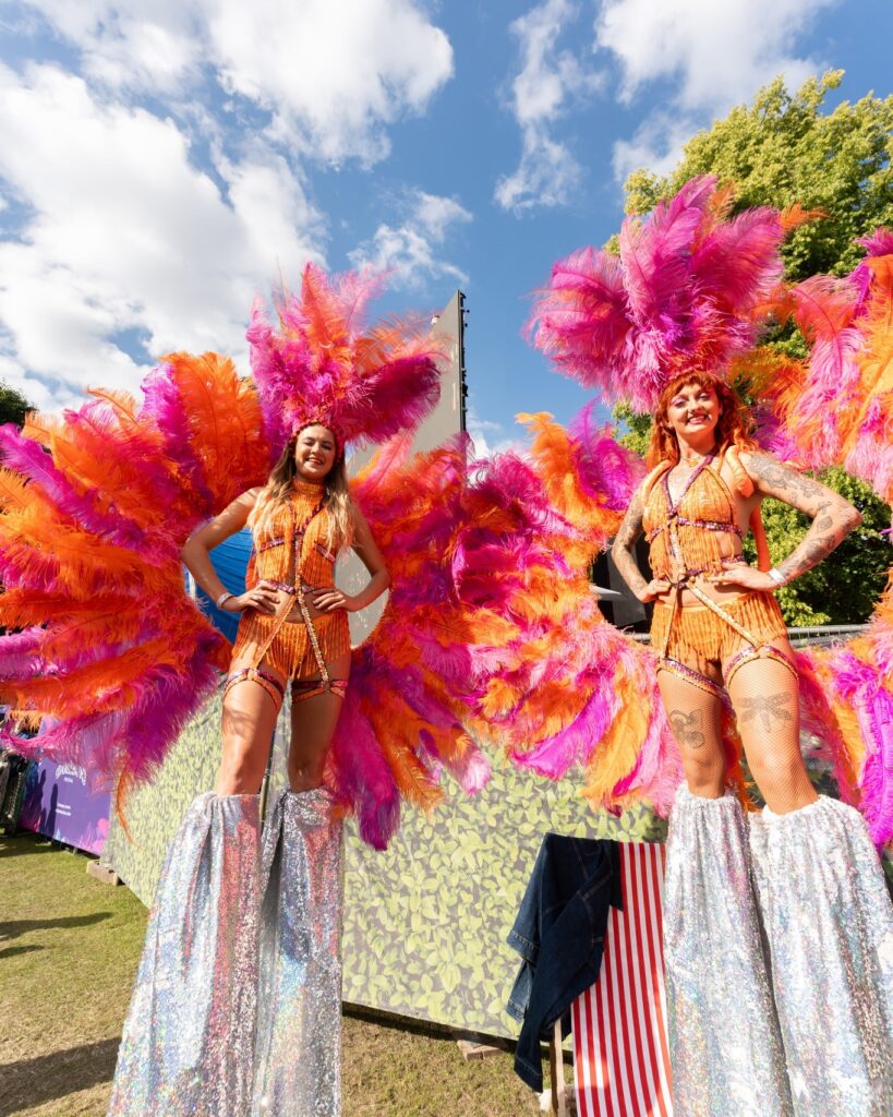 stilt walkers wearing incredible costumes made of orange and bright pink feather head pieces as well as huge feather wings.